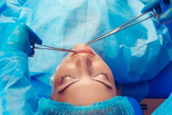 Güzellik uzmanı el dudak cerrahisi araçları kadın ağız yakın tutarak sonuçları kontrol sonra kapatın. Elinde cımbız ve makas var. Güzel kadın gözleri kapalı yordamı alıyor