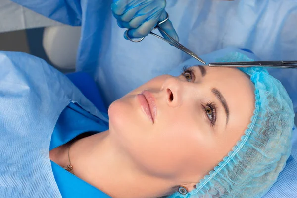 Upper eyelid blepharoplasty. Beautiful middle age woman getting ready for eyelid lift plastic surgery doctor hands in blue gloves point medical tools to her eye. Beauty, people and health concept