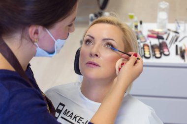 Olgun 49 yaşında bir kadın, güzel alma kadın makyaj. Kozmetik rimel fırçası kadın yüzüne alt kirpik güzellik salonu salonunda rimel uygulamak tutan makyöz yan görünüm 