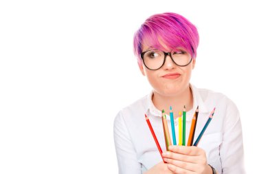 Huysuz olan kadın gözlük ve renkli kalemler kümesi tutarak ve uzak beyaz arka plan üzerinde izole hayal kırıklığı seyir gömlek giymiş pembe saç modeli. Düşünceli sanatçı ressam kavramı.