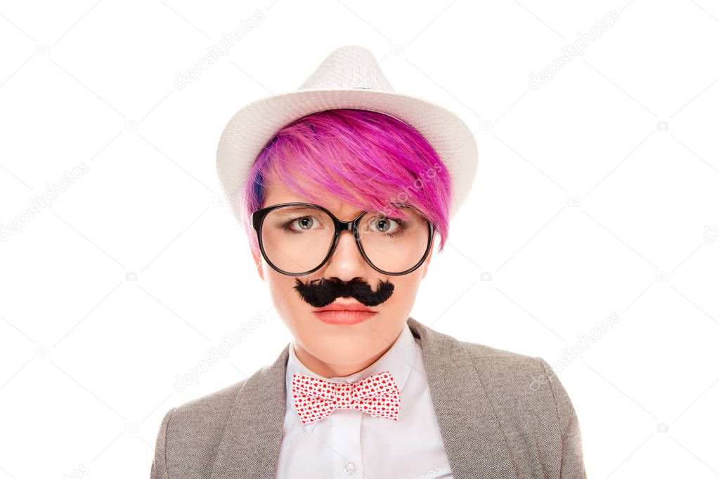 Pretty millennial woman with pink short hair wearing hat with glasses and fake mustache looking seriously at camera isolated on white background 