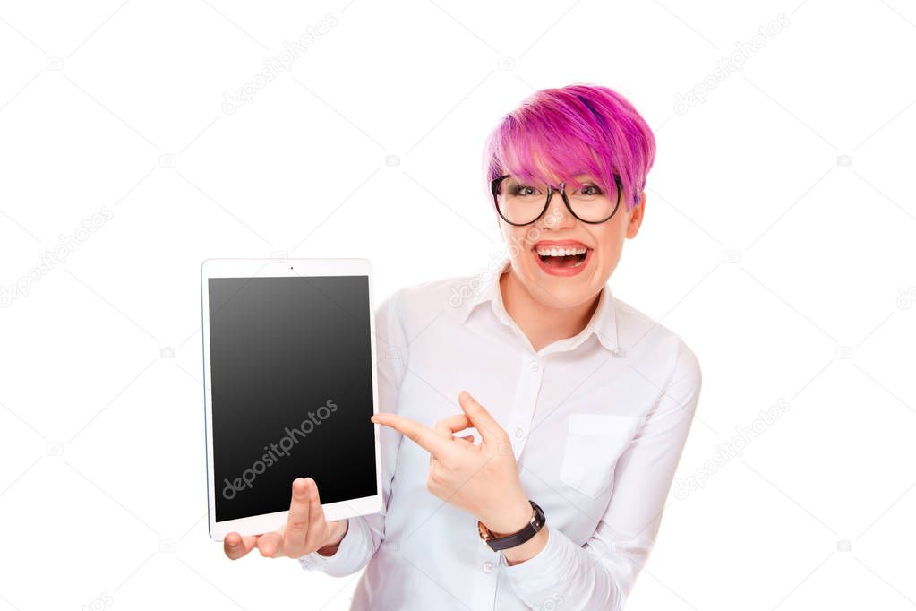 Attractive young excited woman pointing with finger hand at her pad computer standing isolated on white background smiling happy laughing. Millennial model with pink magenta hair.