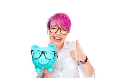 Pembe boyalı saçlı gözlüklü ve beyaz arka plan üzerinde izole bardaklarda mavi kumbara tutarken başparmak gösterilmesini çekici genç kadın