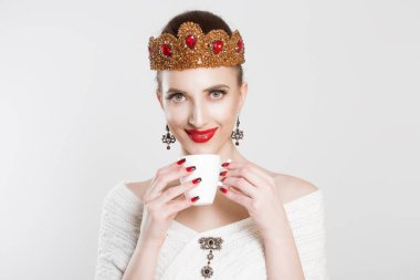 Onun fincan kahve çay keyfi. Gülümseyen güzellik kraliçesi prenses gelin güzel kadın, beyaz sıcak içecek bir fincan elinde olmak beyaz gri arka duvarda izole. Sana bakarken kamera zevk içecek.