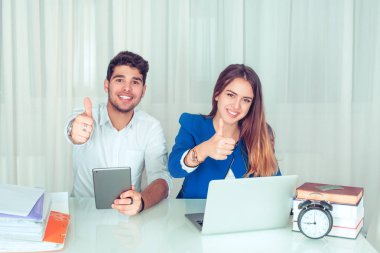 Modern akıllı çift arkadaşları erkek ve kadın başparmak gösterilmesini ve evde oturma odasında masada oturan kamera gülümseyen Ofis masaları gadget'lar ile. Serbest çalışma mutlu işçi kavramı