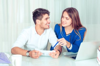 Erkek ve kadın birbirine takım kağıt üzerinde çalışırken bakarak gülümseyen genç. Evde ofis oturma odasında masada oturma çalışma mutlu çift arkadaşları paylaşımı. İş yeri kavramı, romantik aşk