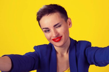 Göz kırpıyor, selfie vurdu. Hareket eden telefon fotoğraf makinesi üzerinde bir selfie yaparken Closeup kadın kısa saçlı kız çocuk hem gülümseyen yanıp sönen göz sarı arka plan izole. Mutlu bir hayat resimleri, mutluluk