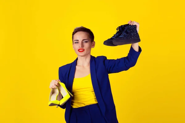 美丽的女人选择在黄色背景墙上的高跟鞋上的平鞋 现代女孩更爱舒适 选择舒适的鞋概念 黄色衬衫和蓝色西装的模特 — 图库照片