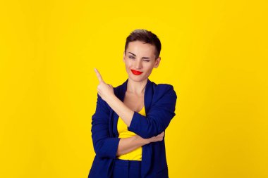 Yanıp sönen göz kırpıyor kadın işaret parmağı üzerinde sarı arka plan izole yan isteyen alan kopyalamak için gösteren göz. Sarı gömlek ve mavi elbise modeli. Olumlu insan duygu, yüz ifadesi.