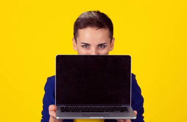 Yetişkin işkadını kısa saç stili kız görüntülenirken laptop boş siyah perde ile orta buraya bak şeklindeki sarı arka plan yarım yüz arkasında saklanıyor izole. Stüdyo yatay görüntü