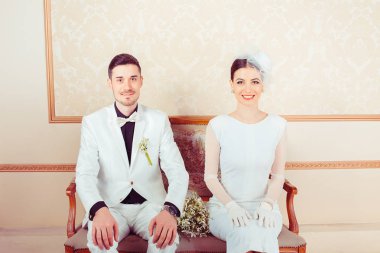 Gelinlik giymiş zarif bir kadın ve erkek koltukta oturmuş kameraya bakıyorlardı.