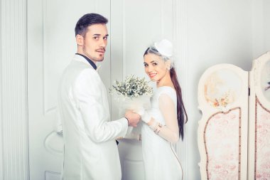 Zarif genç erkek ve kadın el ele tutuşarak ve kameraya bakarak Gelinlikler 