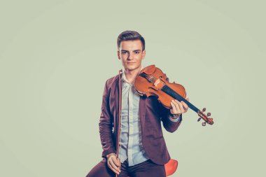 Kameraya bakarak Klasik keman ile sandalyede oturan zarif ceketli genç yakışıklı adamı