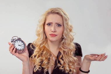 Güzel sarışın şüpheli kadın çalar saat holding, omuzlarında shrugging kameraya bakarak portresi yani ne izole jest beyaz gri arka plan eller bilmiyorum. İnsan yüzü ifade duygu