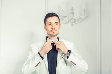 Yakışıklı kendine güvenen genç adam zarif giyen uygun damat yaka çiçeği ve beyaz papyon ayarlama