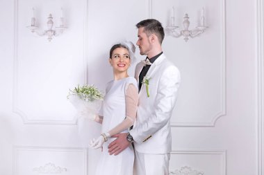 İçerik gelin ve damat birbirlerinin kucaklama beyaz arka plan üzerinde ayakta moda düğün kıyafetleri giyen bakarak