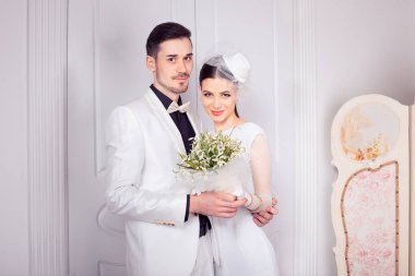 Güzel genç kadın ve adam embrace ayakta düğün ve birlikte kamera poz seyir için şık beyaz kıyafetler içinde