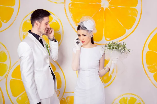 Trendy young happy man and sad woman in wedding outfits speaking on phones and looking at each other