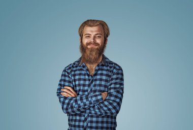 Emin genç gülümseyen adam portresi. Mavi Kareli sakallı hippi erkek forması mavi stüdyo arka plan Isolated damalı. Negatif yüz ifadesi, insan duygu, beden dili, reaksiyon.