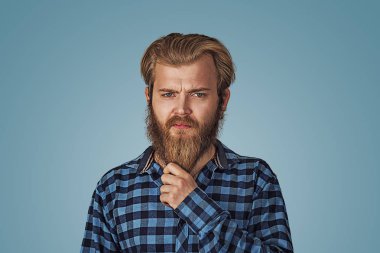 Sakallı şık yakışıklı emin mükemmel saç adamın fotoğraf gösterileri sakal tutar. Mavi Kareli sakallı hippi erkek forması mavi stüdyo arka plan Isolated damalı. Negatif yüz ifadesi