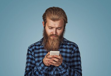 Adam cep telefonu kullanırken çapraşık ve şüpheci arıyor. Mavi Kareli sakallı hippi erkek gömlek izole mavi stüdyo arka plan damalı. Negatif yüz ifade insan duygu beden dili.
