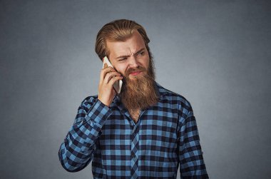 Adam baş ağrısı ile telefonda. Bir telefonda konuşurken mutsuz adam üzgün. Hücresel telefon radyasyon kavramı. Mavi ekose kareli gömlekli Isolated gri gri studio arka plan üzerinde sakallı hippi erkek.