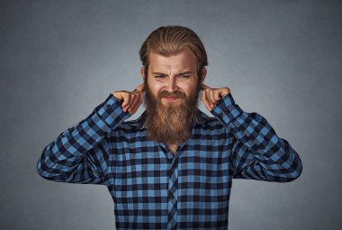 Parmak ile kulakları tıkalı Head shot memnun adam dinlemek istemiyor. Mavi Kareli sakallı hippi erkek gömlek Isolated gri gri studio arka plan üzerinde kareli. Negatif yüz ifadesi.
