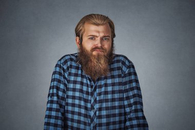 Cehalet ve kibir. Genç adam yani ne umurunda omuzlarında shrugging sakallı. Mavi Kareli sakallı hippi erkek gömlek izole gri gri studio arka plan damalı. Negatif yüz ifadesi.
