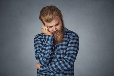 Sad genç adam aşağı bakıyor el ile kafa tutan depresif. Ruh sağlığı kavramı. Mavi ekose kareli gömlekli Isolated gri studio arka plan üzerinde sakallı hippi adam. Negatif yüz ifadesi.