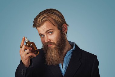 Başarılı bir iş adamı gösterir onun en sevdiği parfüm kokusunu teklif seviyor tercih ediyor. Hipster işadamı Isolated mavi zemin üzerine sakallı. Tarafsız yüz ifadesi, insani duyguları vücut dili tepki