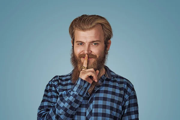 Smiling smug man hipster guy keeps a secret. Confidential information and tips sharing concept. Hipster male with beard in blue plaid checkered shirt  Isolated on blue studio Background. Negative face