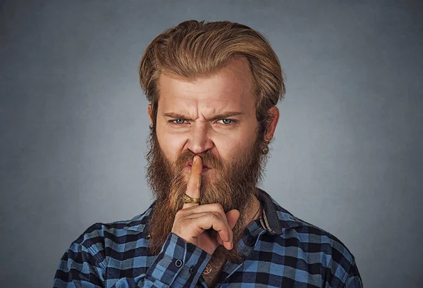 Confident serious angry male, keeps index finger on lips, asking to stay quiet mute. Hipster man with beard in blue plaid checkered shirt  Isolated on gray studio Background. Negative face expression.