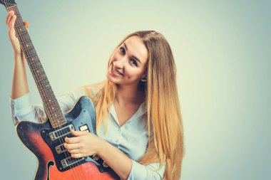 Elektro gitar çalmak ve gri arka plan kameraya gülümseyen coquette genç sarışın kadın