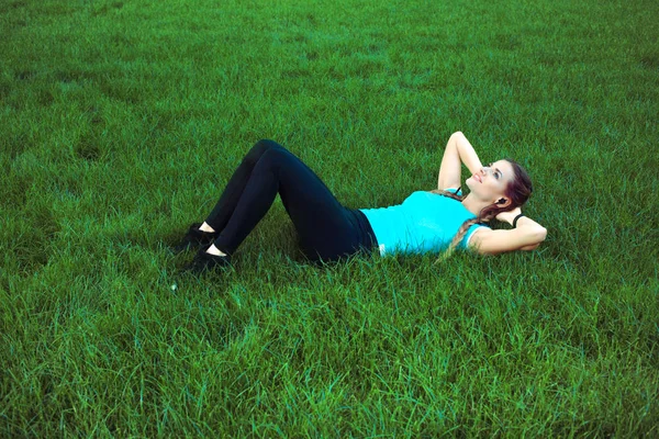 Slim sportive woman training abs on green lawn in park