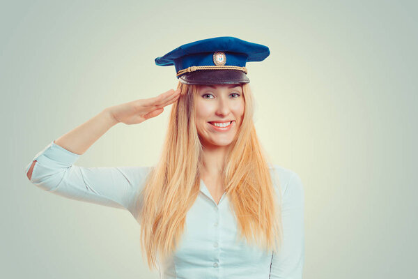 Charming blond woman in blue service cap giving salute at camera and smiling