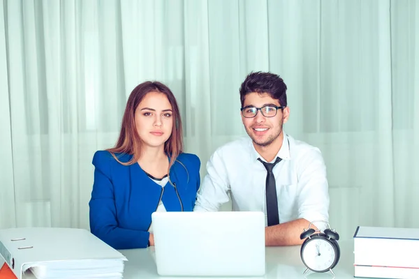 Couple in office behind laptop looking at you camera happy smiling. Business people freelance working at home. Positive face expression human emotion body language reaction attitude. Horizontal shot.