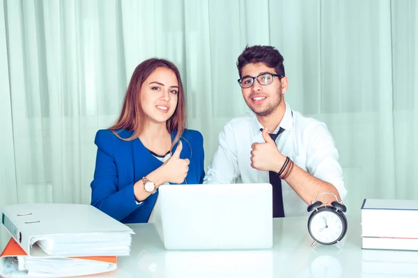 Cheerful modern smart couple colleagues man, woman with laptop at office table showing thumbs up like and smiling at camera sitting at table in living room at home Freelance work happy workers concept