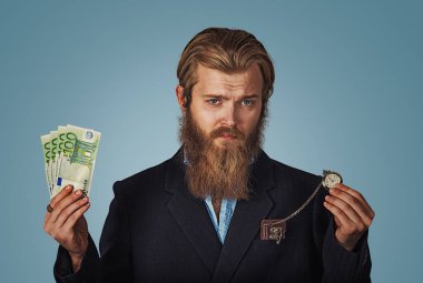 Para kavramı zamanı. Yakışıklı sakallı hippi ciddi iş adamı adam nakit para birimi ve retro cep Isolated mavi zemin üzerine dikkat et. Negatif yüz ifade insan duygu beden dili