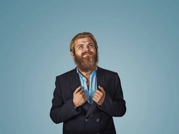 Bearded hipster business man hands on suit showing super hero shirt rising his head looking up and smiling Isolated on blue Background. Negative face expression, human emotion, body language, reaction