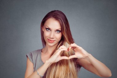 Bir kalp jest yapmak oldukça romantik genç kadın parmakları ile arka plan gri gri stüdyo duvarda izole mutlu ihale gülümseme ile onun aşk ve sevgi gösteren eller. Pozitif yüz ifadesi