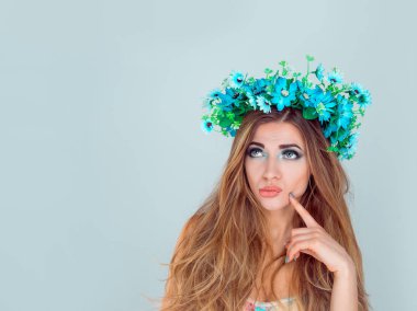 Düşünceli şüpheci şüpheli şaşkın olan kadın çiçek kafa bandı tarafına bakıyordum. Baş şüpheli üzerinde mavi arka plan ile boşaltmak izole üzerinde çiçek çiçek taç ile kız moda