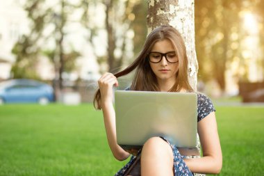 Genç kadın, öğrenci, açık havada yeşil çim kulaklıklar kafasına oturarak dışında bir dizüstü bilgisayar kullanarak genç. Çok kültürlü modeli, karışık ırk, Asyalı Rus kız. Uzay kopyalayın. İnsan ve teknoloji.