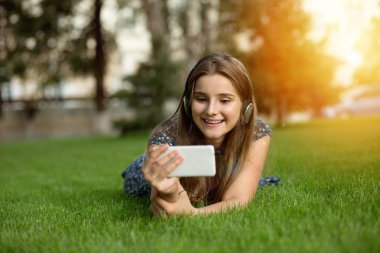 Arayan kadın kablosuz kulaklıklar açık havada baş kulaklıktan yeşil çim üzerinde yalan kafasına bir smartphone cep telefonu ile bir müzik video. Çok kültürlü modeli, karışık ırk, Asyalı Rus kız. Kopya alanı. 