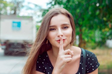 Shh Woman wide eyed asking for silence or secrecy with finger on lips hush hand gesture city park outdoor background Pretty girl placing fingers on lips sign symbol. Positive emotion facial expression clipart