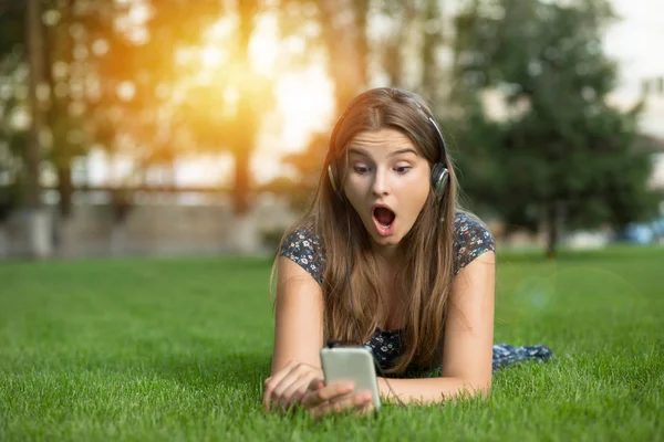 Şok kadın açık havada baş kulaklıktan yeşil çim üzerinde yalan Internet tarafından şok haber okuma kafasına telefon kulaklık arıyorum. Çok kültürlü modeli karışık ırk, Asyalı Rus kız. Kopya alanı