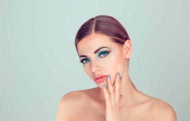 Seksi kadın manikür seti makyaj ile gösteren el ile yüz dokunmadan. Mavi yeşil göz gölgeler makyaj ve ışık yeşil gri arka plan üzerinde izole manikür çekici genç model.