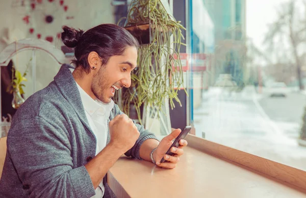 Hombre eufórico bombeando puño mientras mira el teléfono inteligente móvil . — Foto de Stock