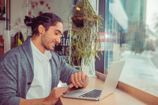 Homem sorrindo olhando para relógio de pulso enquanto trabalhava no computador . — Fotografia de Stock