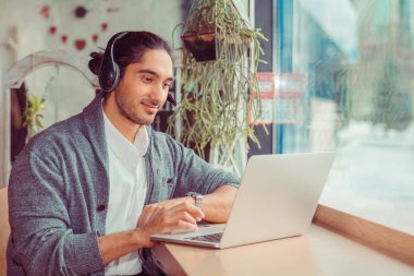 dizüstü bilgisayar ve müzik dinleme kullanarak kafede sakallı genç adam öğrenci.