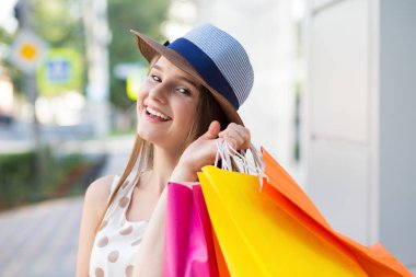 Size kamera bakarak alışveriş torbaları tutan mutlu kadın